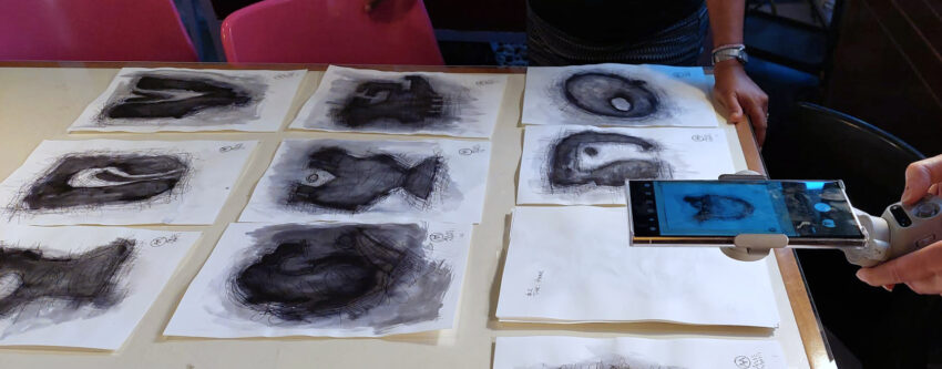 images on paper spread in rows on a table and phone photographing them